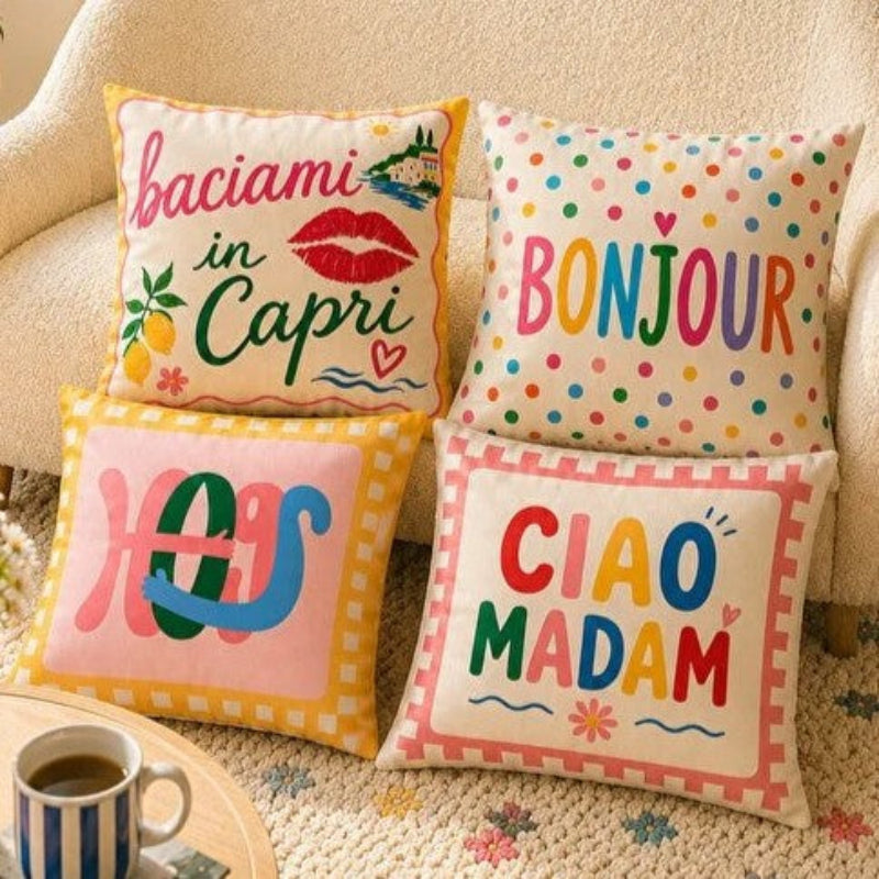 Set of four colorful Capri-inspired decorative cushion covers featuring playful typography and Mediterranean-inspired designs arranged on a cozy armchair.