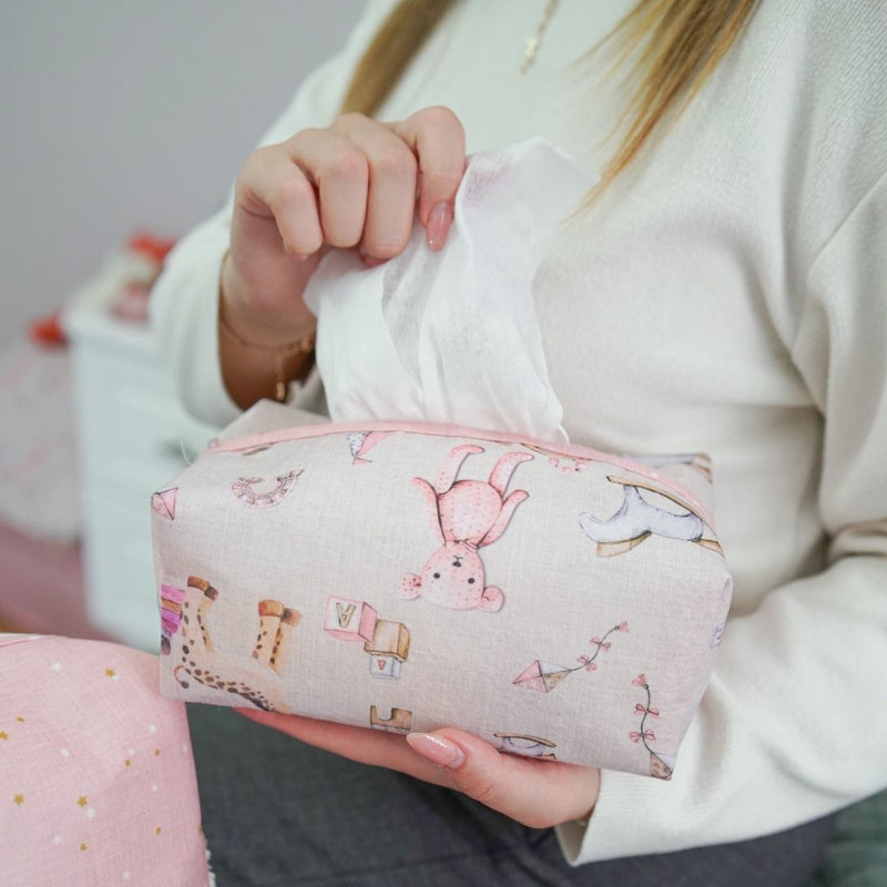 Pink baby nursery organizer set with decorative tissue box cover and zippered storage pouch placed on bed