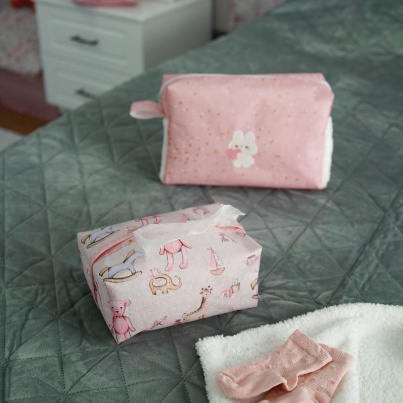 Pink baby nursery organizer set with decorative tissue box cover and zippered storage pouch placed on bed
