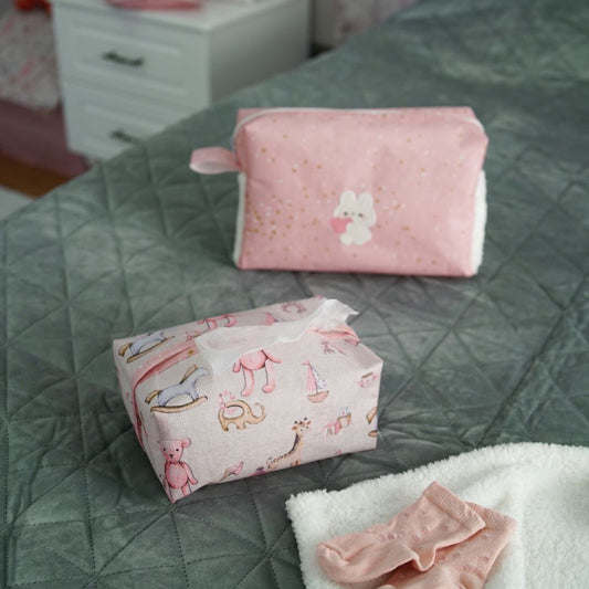 Pink baby nursery organizer set with decorative tissue box cover and zippered storage pouch placed on bed
