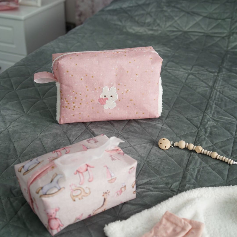 Pink baby nursery organizer set with decorative tissue box cover and zippered storage pouch placed on bed