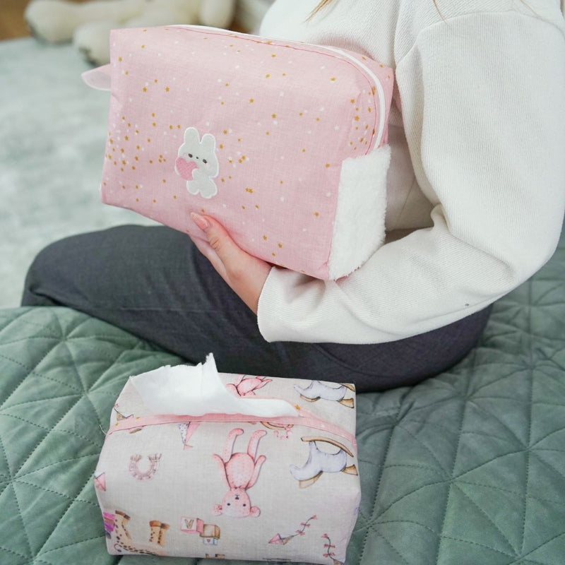 Pink baby nursery organizer set with decorative tissue box cover and zippered storage pouch placed on bed