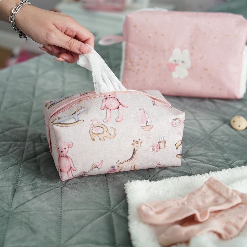Pink baby nursery organizer set with decorative tissue box cover and zippered storage pouch placed on bed
