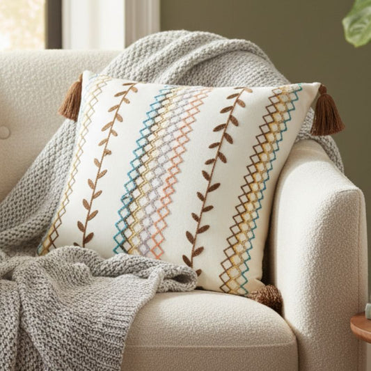 Square boho cushion cover with multi-color embroidered geometric and leaf pattern, finished with brown tassels on all four corners, 43x43 cm