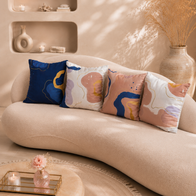Warm neutral cushion cover with abstract shapes in beige, blue, and gold tones on a decorative pillow