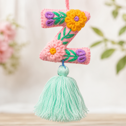 Handmade embroidered letter Z ornament with colorful floral stitching and light green tassel on wooden background