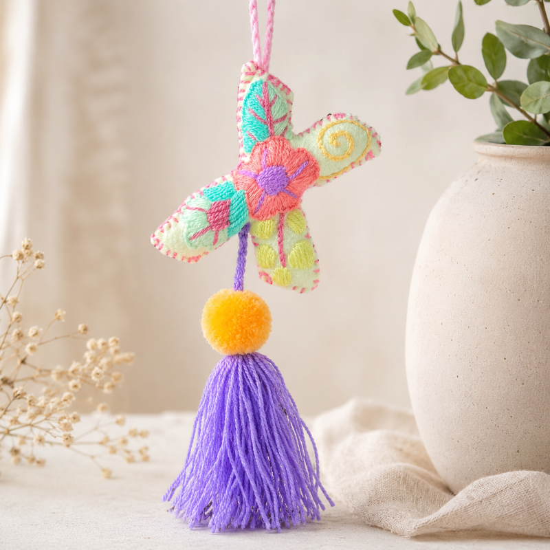 Colorful handmade embroidered letter X ornament with floral patterns, yellow pom pom and purple tassel on wooden background