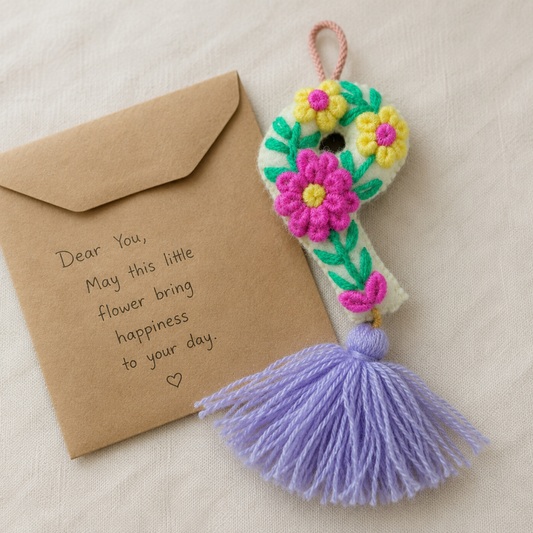 Handmade embroidered letter P ornament with colorful floral embroidery and lavender tassel on wooden background