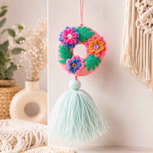 Handmade embroidered letter O ornament with colorful floral embroidery and mint green tassel on wooden background