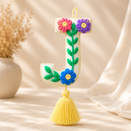 Handmade embroidered letter F ornament with floral patterns and yellow tassel on wooden background