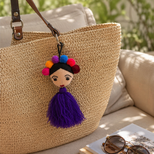 Handmade Frida-inspired doll charm with colorful pom-poms and purple tassel attached to teal bag