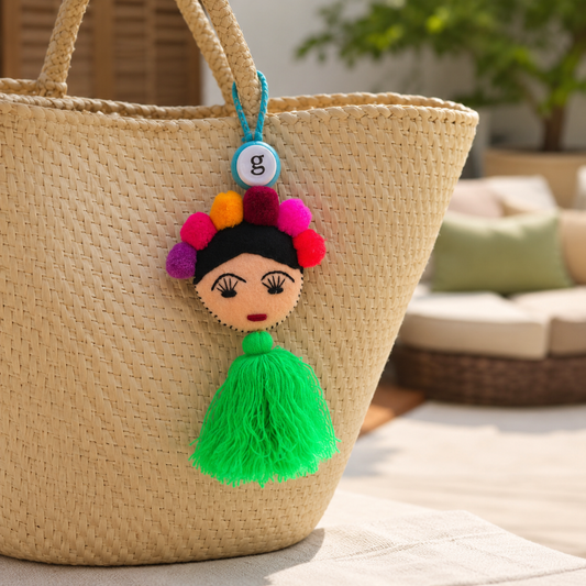 Handmade Frida-inspired doll charm with colorful pom-poms and green tassel attached to teal bag