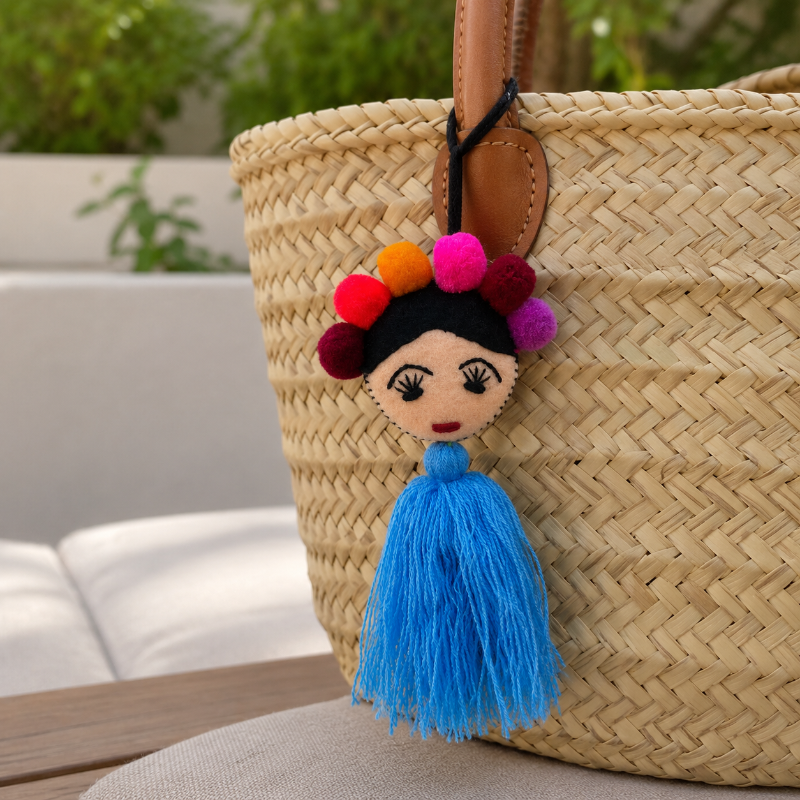 Handmade Frida-inspired doll ornament with colorful pom-poms and blue tassel attached to teal bag