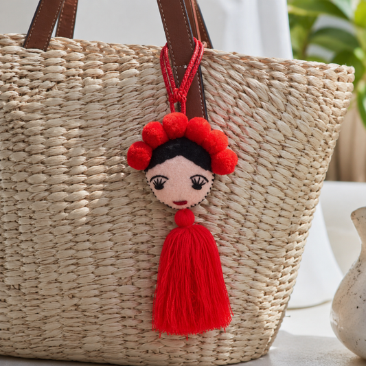 Handmade Frida-inspired doll charm with red pom-poms and red tassel on teal bag