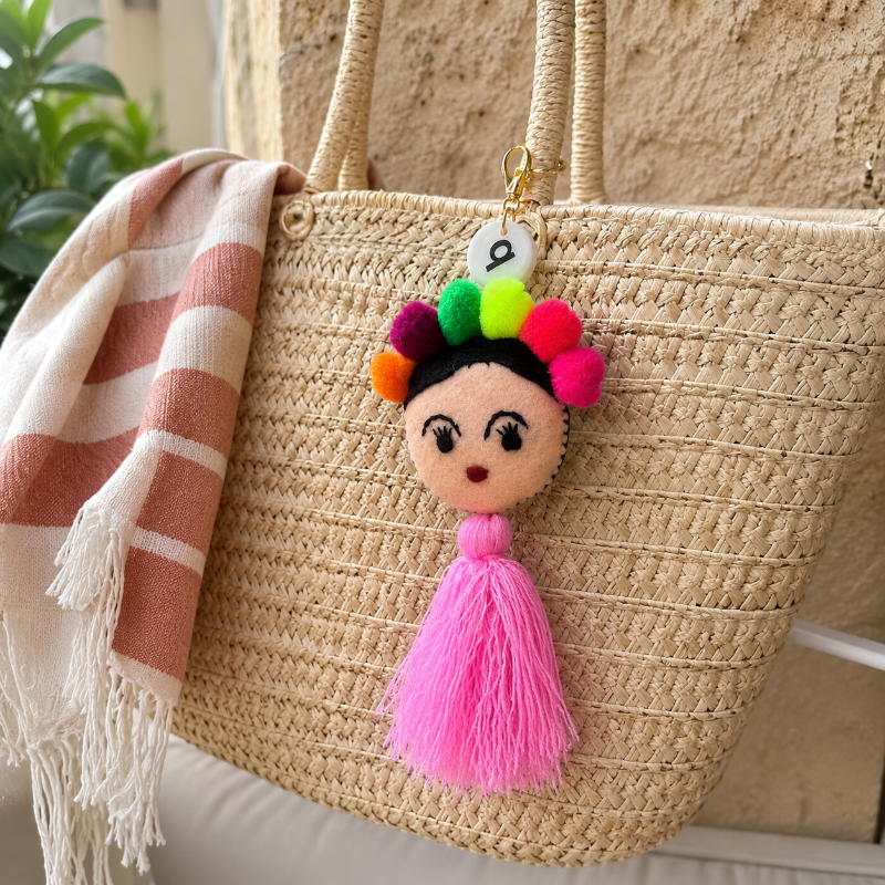 Handmade Frida-inspired doll charm with colorful pom-poms and soft pink tassel on teal bag
