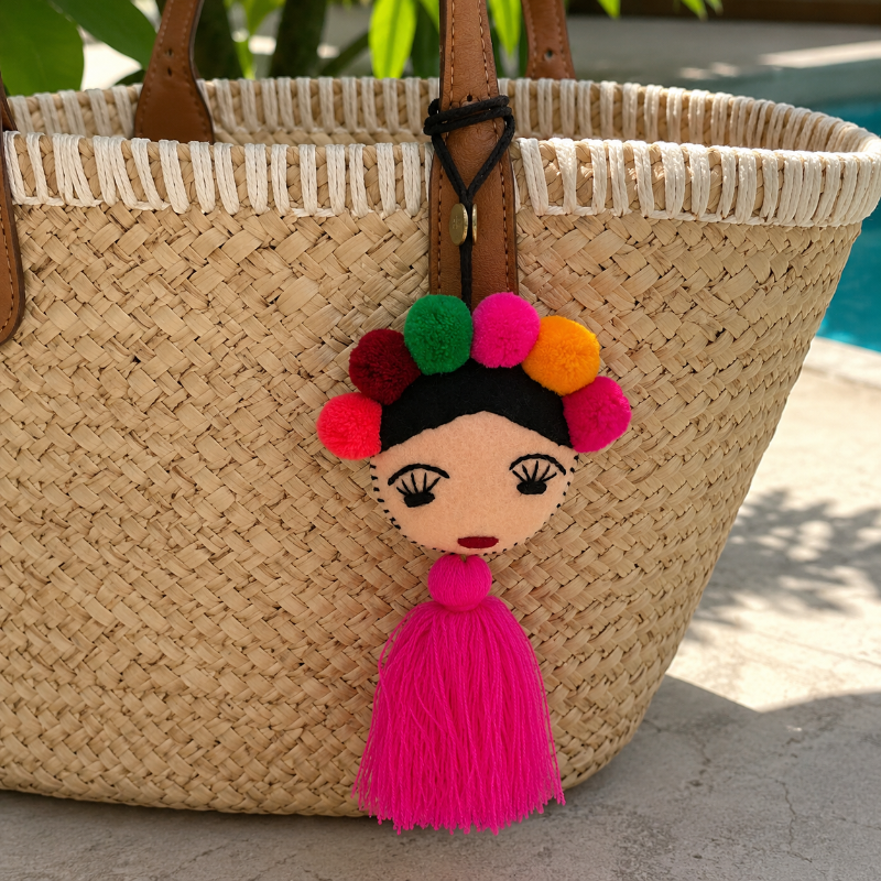 Handmade Frida-inspired doll charm with colorful pom-poms and pink tassel on teal bag