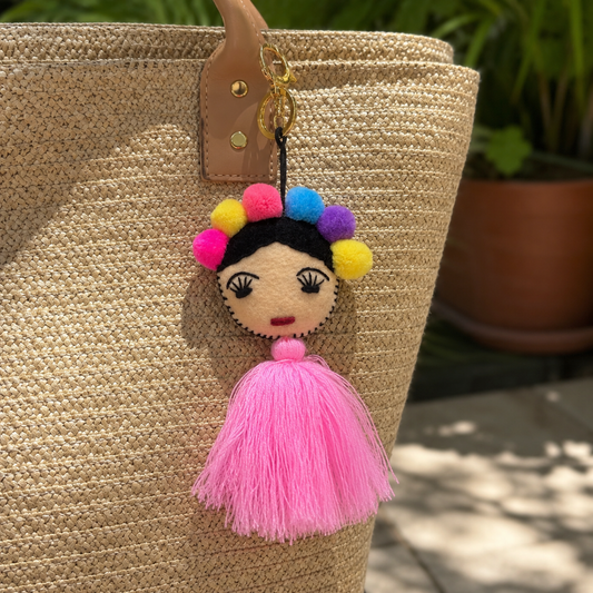 Handmade Frida-inspired doll charm with colorful pom-poms and light pink tassel on teal bag