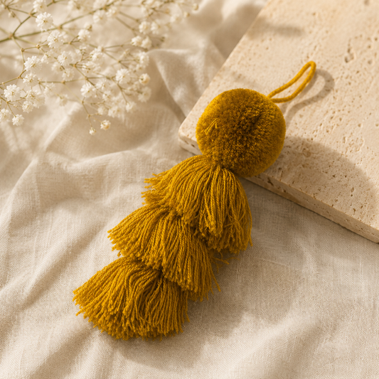Mustard yellow fluffy tassel keychain with soft pom pom placed on grass background