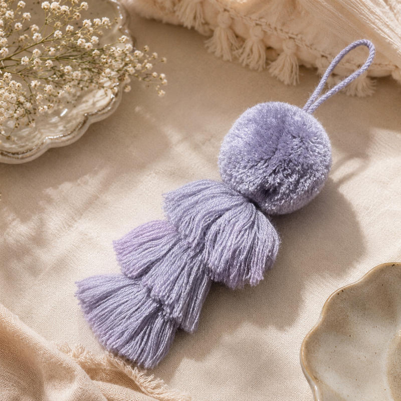 Grey fluffy tassel keychain with soft pom pom placed on grass 