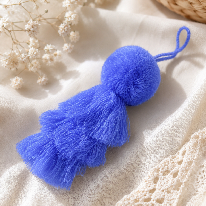 Purple fluffy tassel keychain with soft pom pom placed on grass 