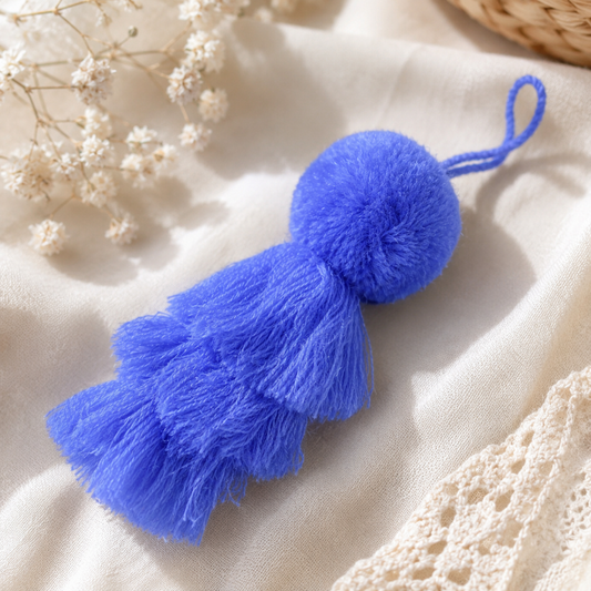 Purple fluffy tassel keychain with soft pom pom placed on grass 