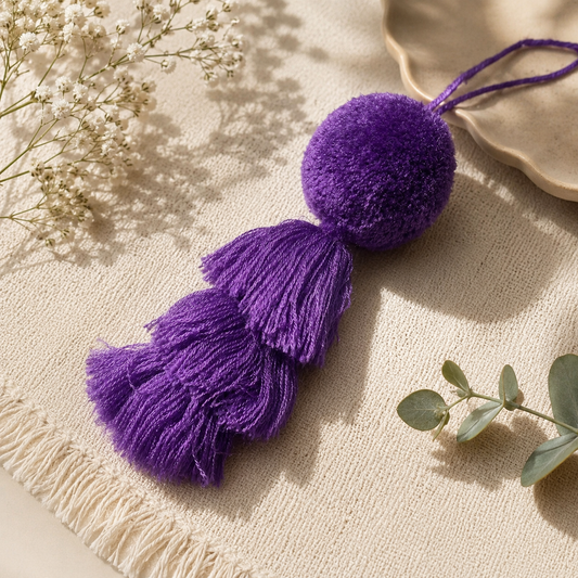 Dark purple fluffy tassel keychain with soft pom pom placed on grass background