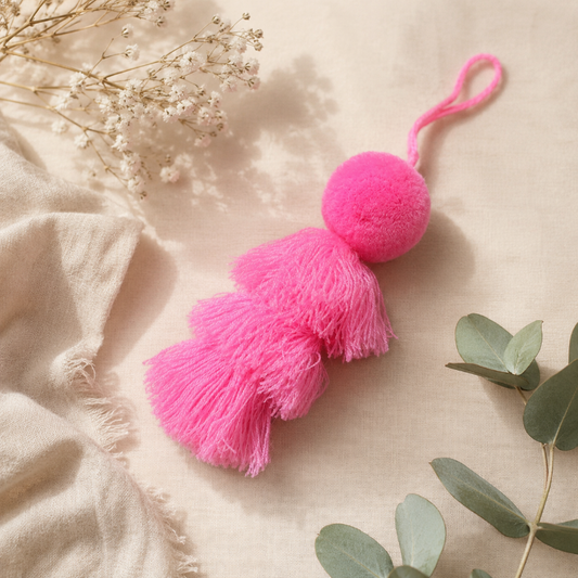 Pink fluffy tassel keychain with soft pom pom placed on grass 