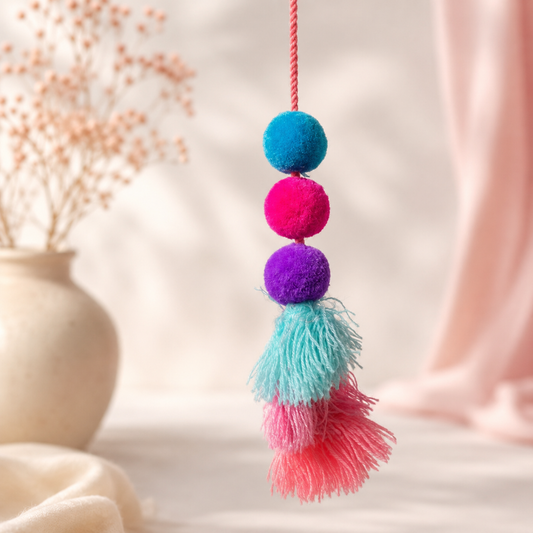 Handmade pom pom tassel hanging decor with colorful pom poms and layered pastel yarn tassels on white door background