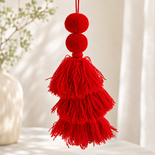 Classic red pom-pom tassel hanging decoration with two pom-poms and layered red yarn tassels hanging on a wooden chair.