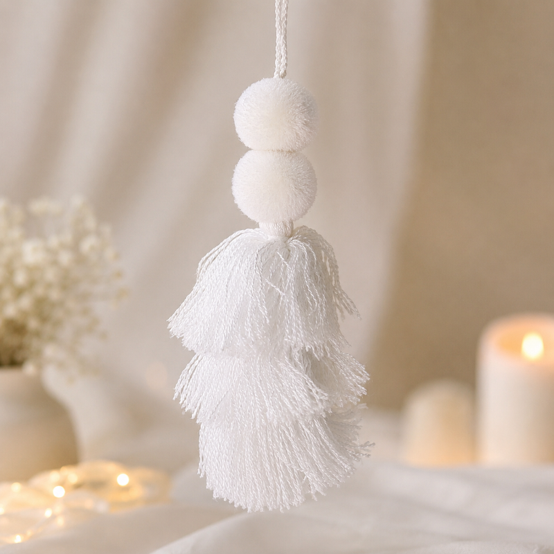Minimalist white pom-pom tassel hanging decoration with layered white yarn tassels hanging on a wooden chair.