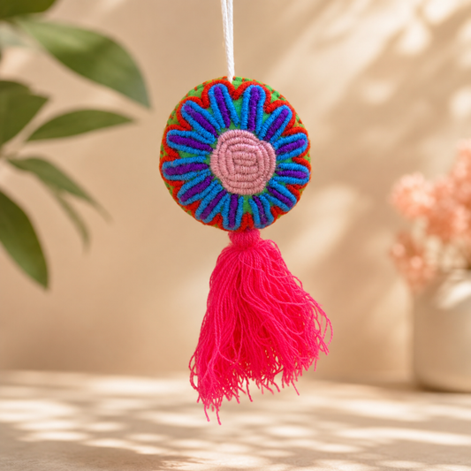 Handmade multicolor embroidered flower ornament with pastel center and red tassel on a yellow 