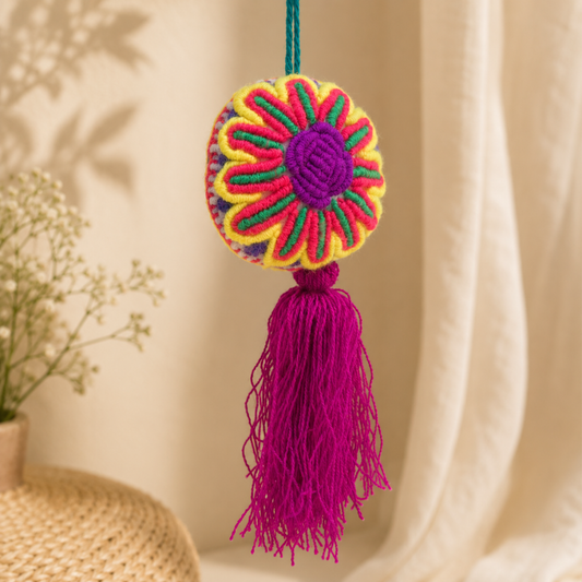 Handmade multicolor embroidered flower ornament with magenta tassel on a yellow background