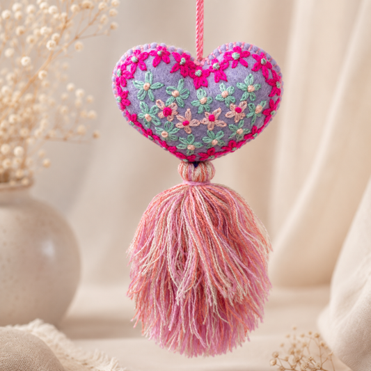 Handmade lavender embroidered heart tassel with colorful floral embroidery and pink yarn fringe on curtain