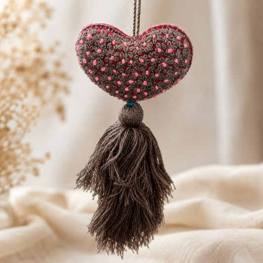 Handmade taupe embroidered heart tassel with pink floral embroidery and brown yarn fringe on curtain