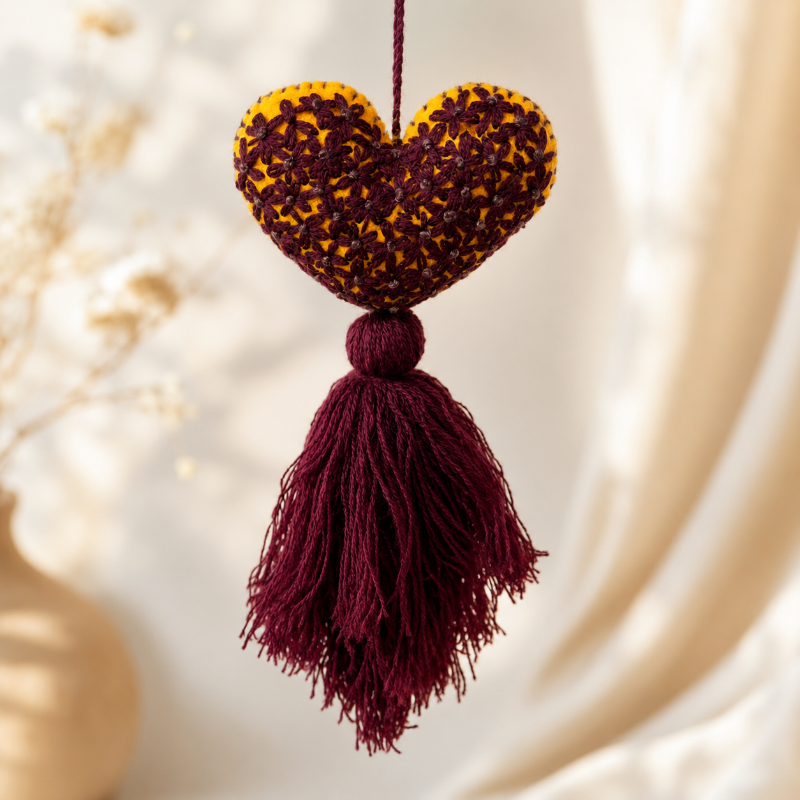 Handmade mustard embroidered heart tassel with burgundy floral stitching and matching yarn fringe on curtain