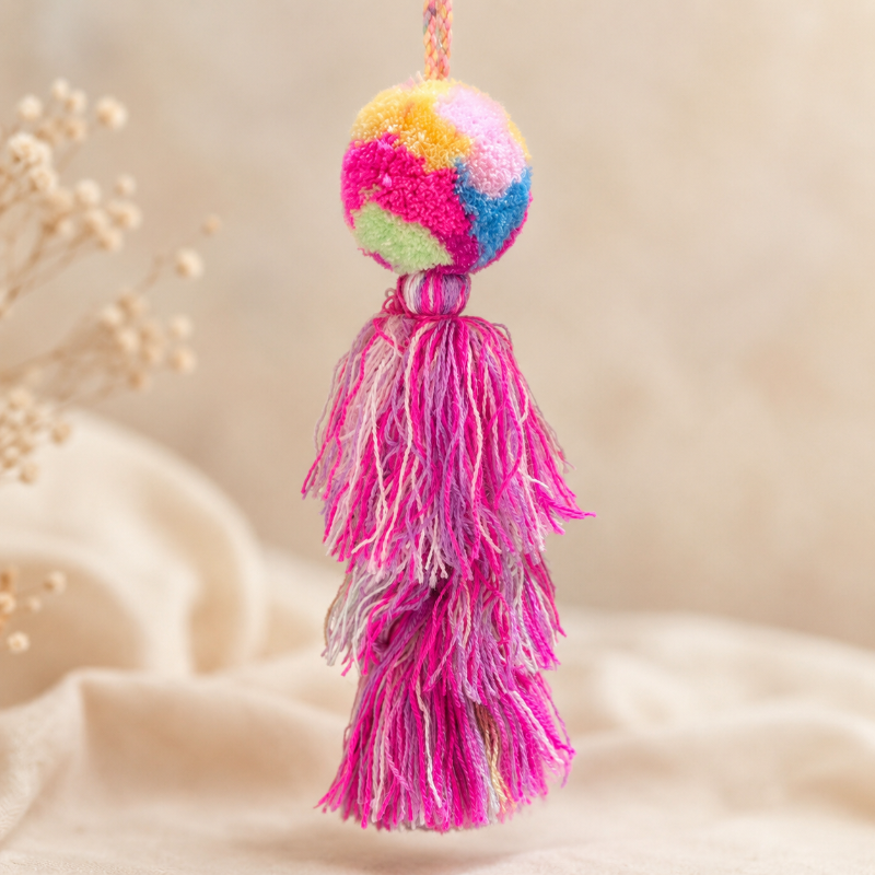 Rainbow pom pom tassel bag charm with layered pink tassels attached to a beige handbag