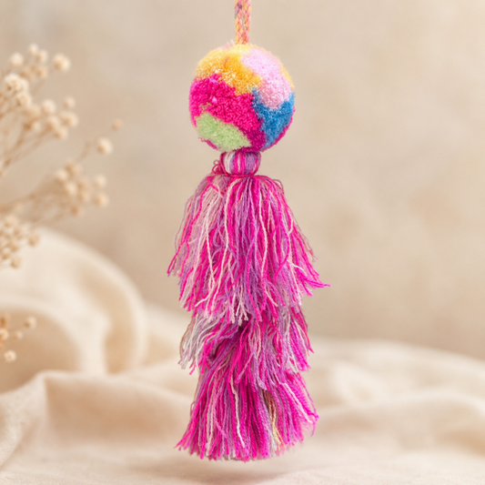 Rainbow pom pom tassel bag charm with layered pink tassels attached to a beige handbag