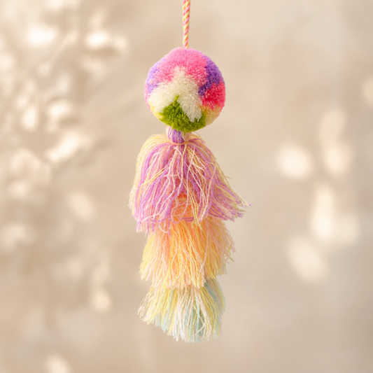 Pastel rainbow pom pom tassel bag charm with soft multicolor tassels attached to a beige handbag