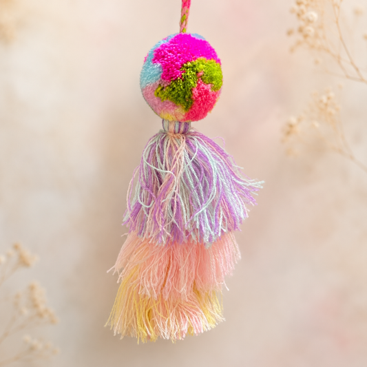 Pastel multicolor pom pom tassel bag charm with layered soft-toned tassels attached to a beige handbag