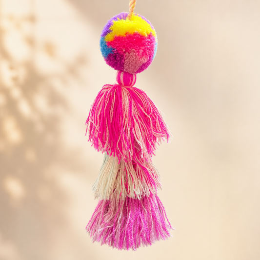 Neon pink pom pom tassel bag charm with layered multicolor tassels attached to a beige handbag