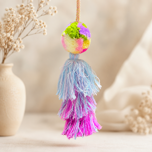 Pastel pom pom tassel bag charm with light blue and pink yarn attached to a beige handbag