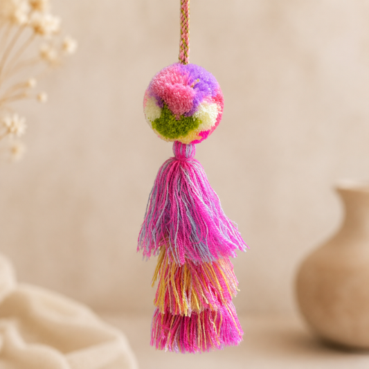 Multicolor pom pom tassel bag charm with pink layered tassels attached to a beige handbag