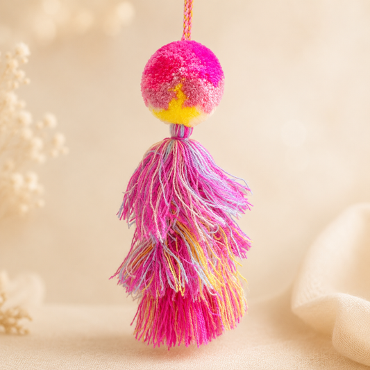 Bright pink pom pom tassel bag charm with layered multicolor tassels attached to a beige handbag