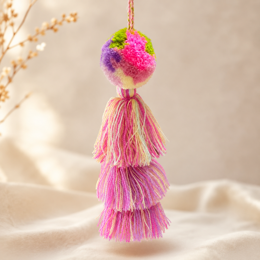 Soft pink pom pom tassel bag charm with layered pastel tassels attached to a beige handbag