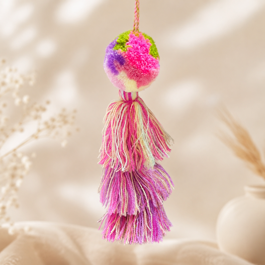 Pink pastel pom pom tassel bag charm with layered soft-toned tassels attached to a beige handbag