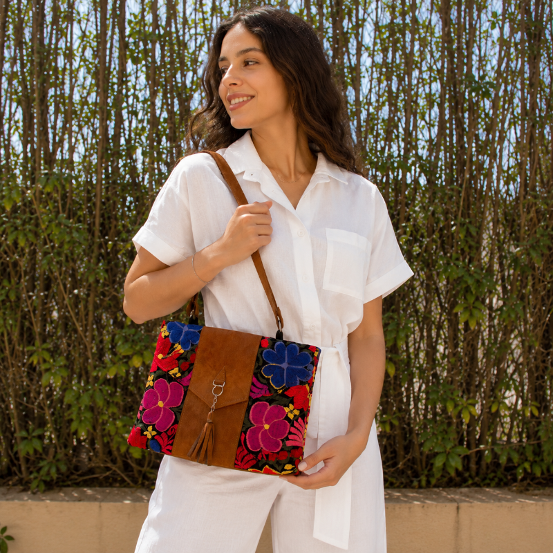 Woman wearing a black floral embroidered crossbody bag with a brown leather panel and tassel detail outdoors