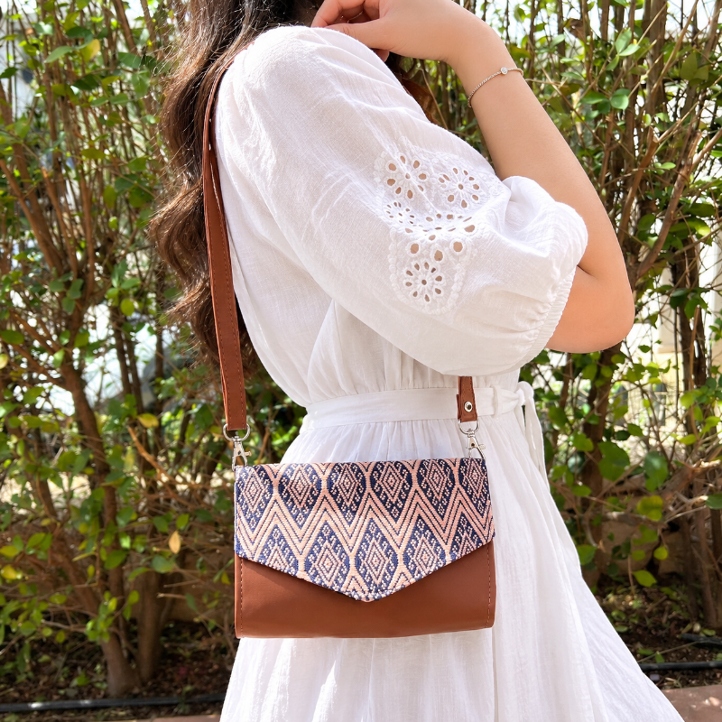 Woman wearing a brown leather crossbody bag with beige and navy geometric woven flap outdoors