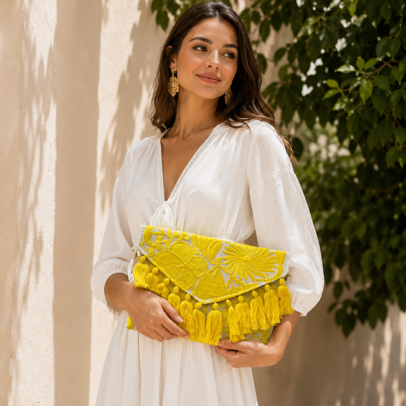 Bright yellow floral embroidered clutch bag with tassels held by a person wearing a brown dress outdoors