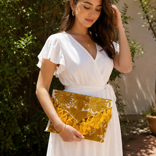 Mustard yellow floral embroidered clutch bag with tassels held by a person wearing a brown dress outdoors