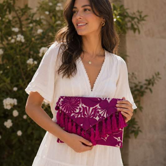 Bohemian pink floral embroidered clutch bag with tassels held by a person wearing a brown dress outdoors